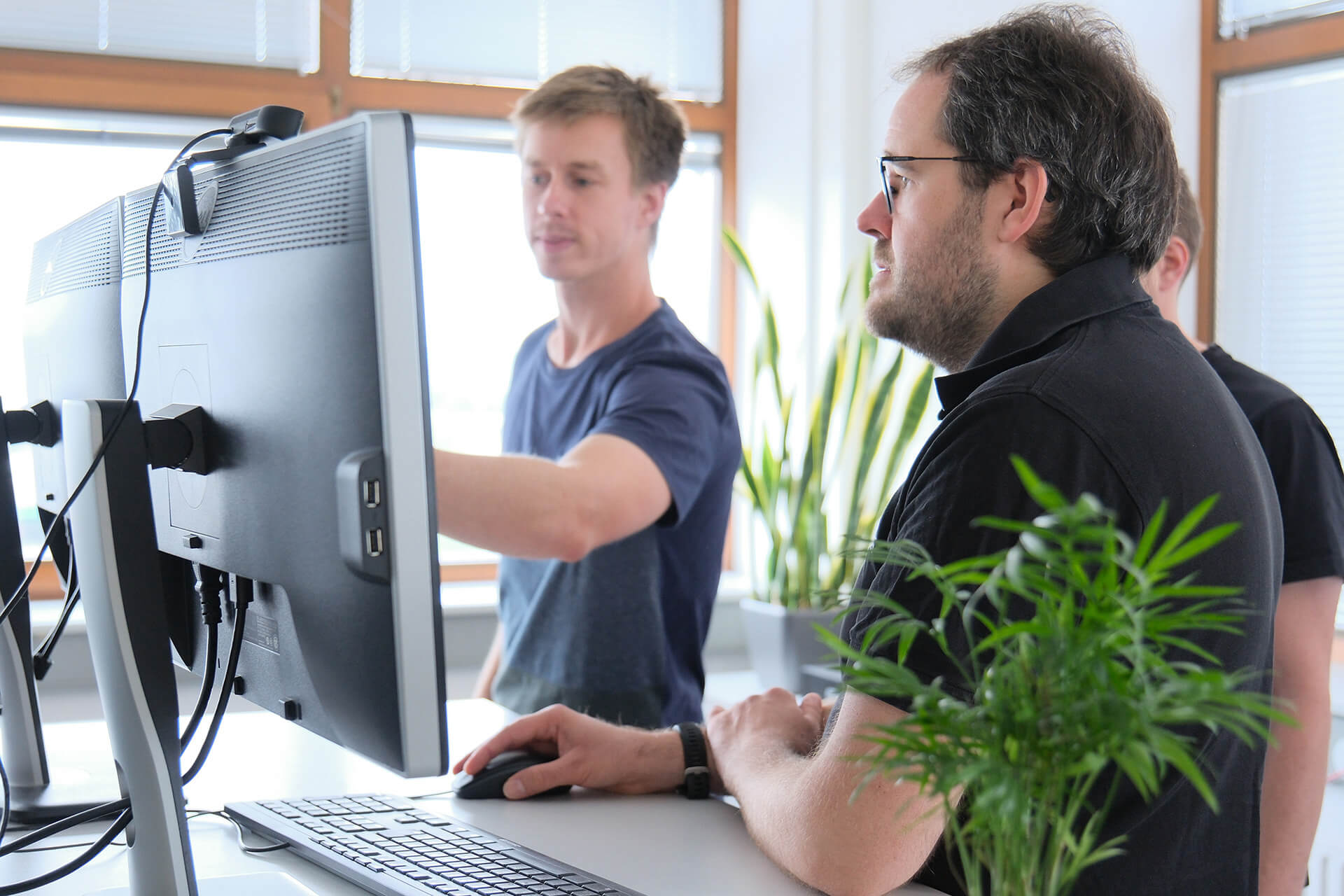 Drei Kollegen stehenvor einem PC; einer zeigt den anderen etwas auf dem Bildschirm.